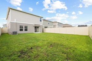 Una propiedad residencial con patio trasero cercado, una casa de dos plantas y cielo despejado.