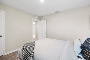 A bedroom with a bed, a checkered throw, and a door leading to another room. - NEW - Cozy & Spacious 4bedroom Retreat! (Wesley Chapel)
