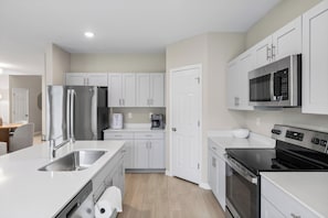 A modern kitchen with stainless steel appliances, white cabinetry, and a wooden floor. - NEW - Cozy & Spacious 4bedroom Retreat! (Wesley Chapel)