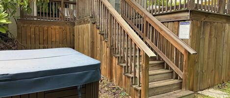 A wooden deck with a hot tub, a wooden staircase, and a safety sign.