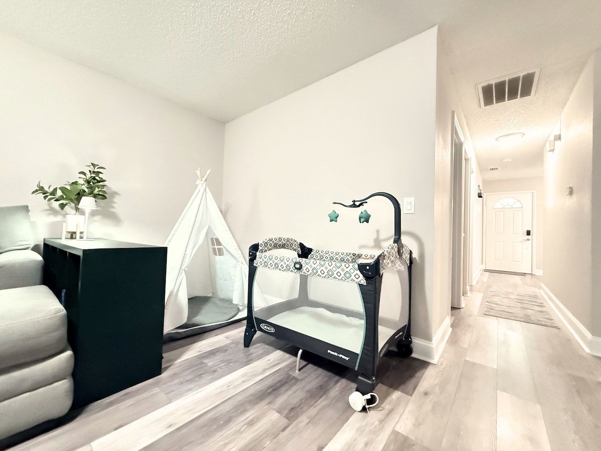 A room with a bed, a playpen, a tent, and a potted plant.