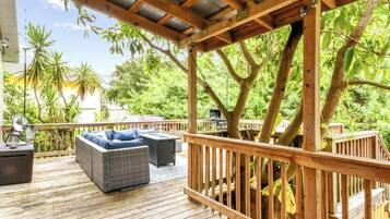 An outdoor deck with wooden railings, a wicker sofa, and a grill area.
