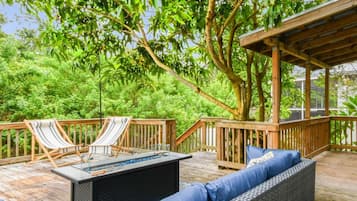 Una terraza de madera con mobiliario exterior, incluyendo un sofá y sillas, rodeada de abundante vegetación.