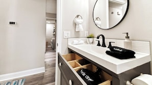 A modern bathroom with a white vanity, a black faucet, a round mirror, and a towel rack. - Charming Home Near Macdill AFB Hot Tub Fire Pit (Tampa)