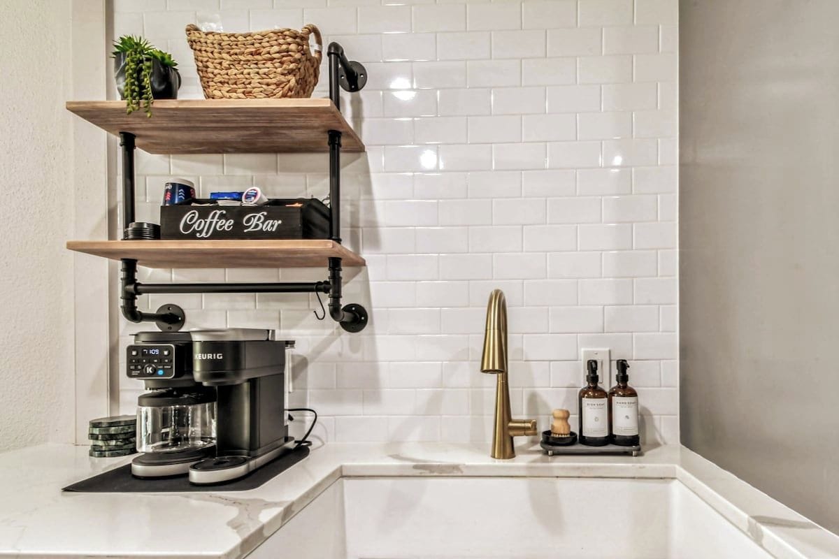 A kitchen with a coffee machine, shelves with a coffee bar sign, and bottles on the countertop.