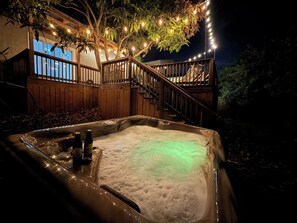 Un jacuzzi con muelle de madera y luces de cadena, rodeado de árboles.