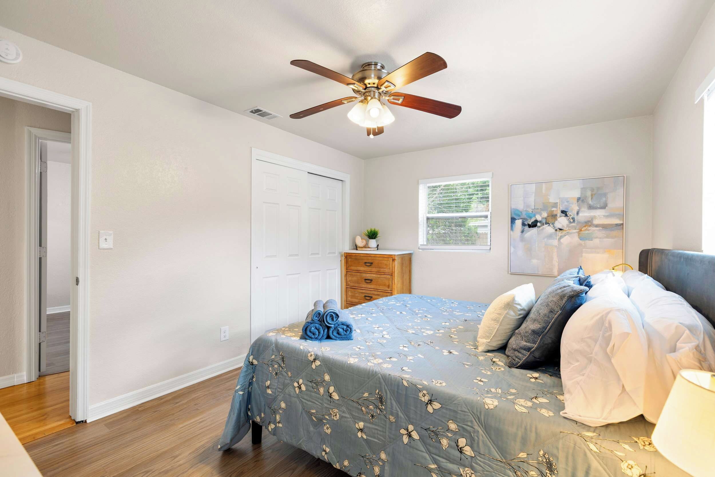 A bedroom with a bed, a ceiling fan, a window, and a door.