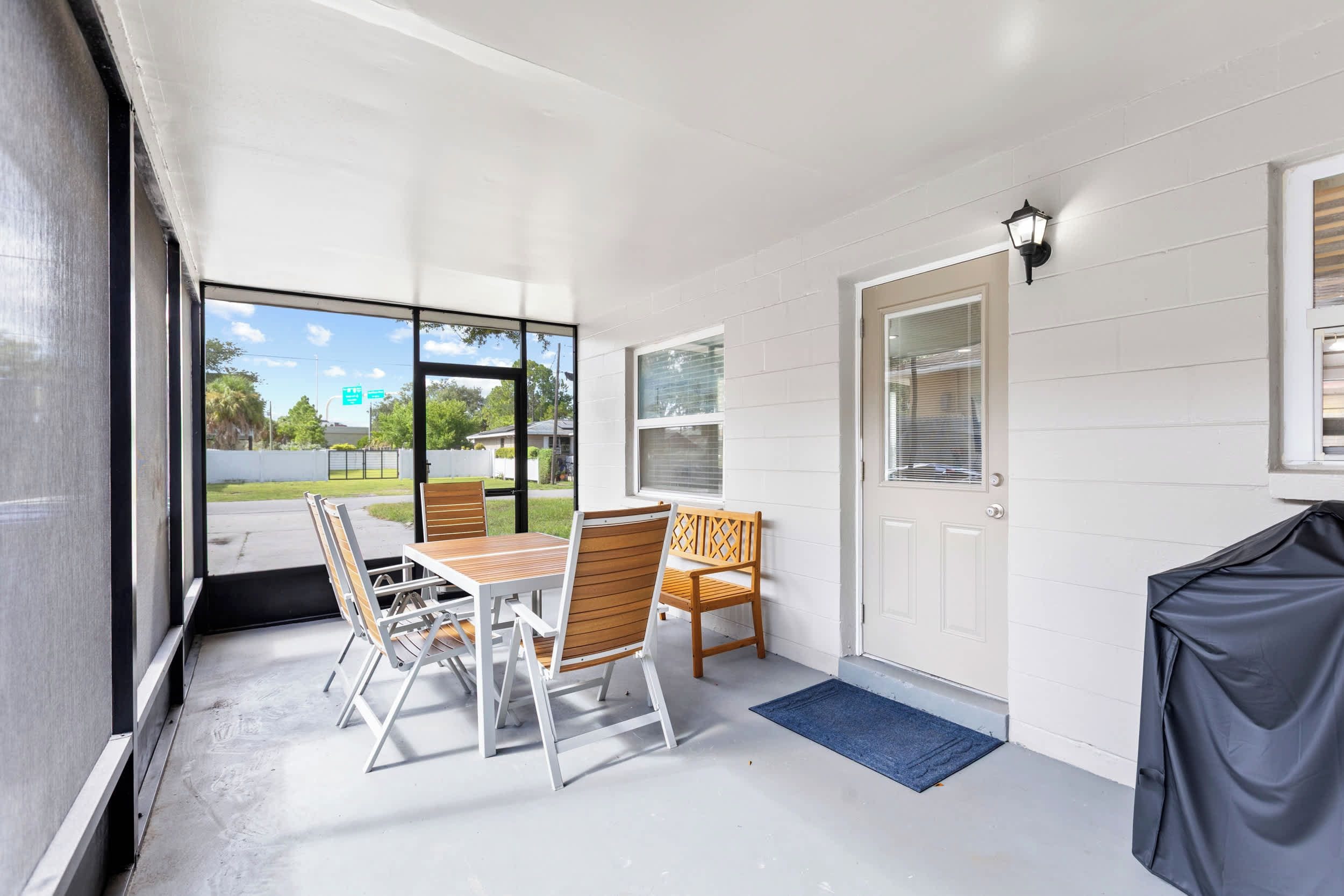 A covered patio with a table and chairs, a door with a window, and a view of the outside.