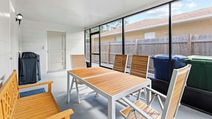 A patio area with a table and chairs, a covered bench, and a view of a backyard with a wooden fence and trash bins. - NEW - 3BD Cozy Downtown Retreat! (Tampa)
