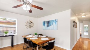A dining area with a wooden table, black chairs, a ceiling fan, and a painting on the wall. - NEW - 3BD Cozy Downtown Retreat! (Tampa)