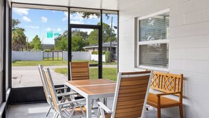 A covered outdoor seating area with a table and chairs, a window with blinds, and a view of a road with a sign. - NEW - 3BD Cozy Downtown Retreat! (Tampa)