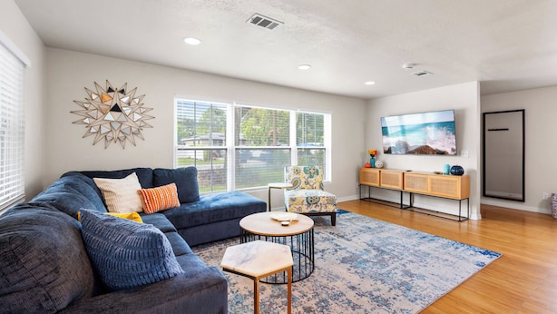A modern living room with a blue sofa, a round coffee table, and a television on the wall. - NEW - 3BD Cozy Downtown Retreat! (Tampa)