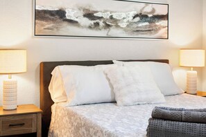 Habitació d'hotel amb un llit, dues làmpades de nit, una tauleta de nit i un quadre abstracte gran a la pared.