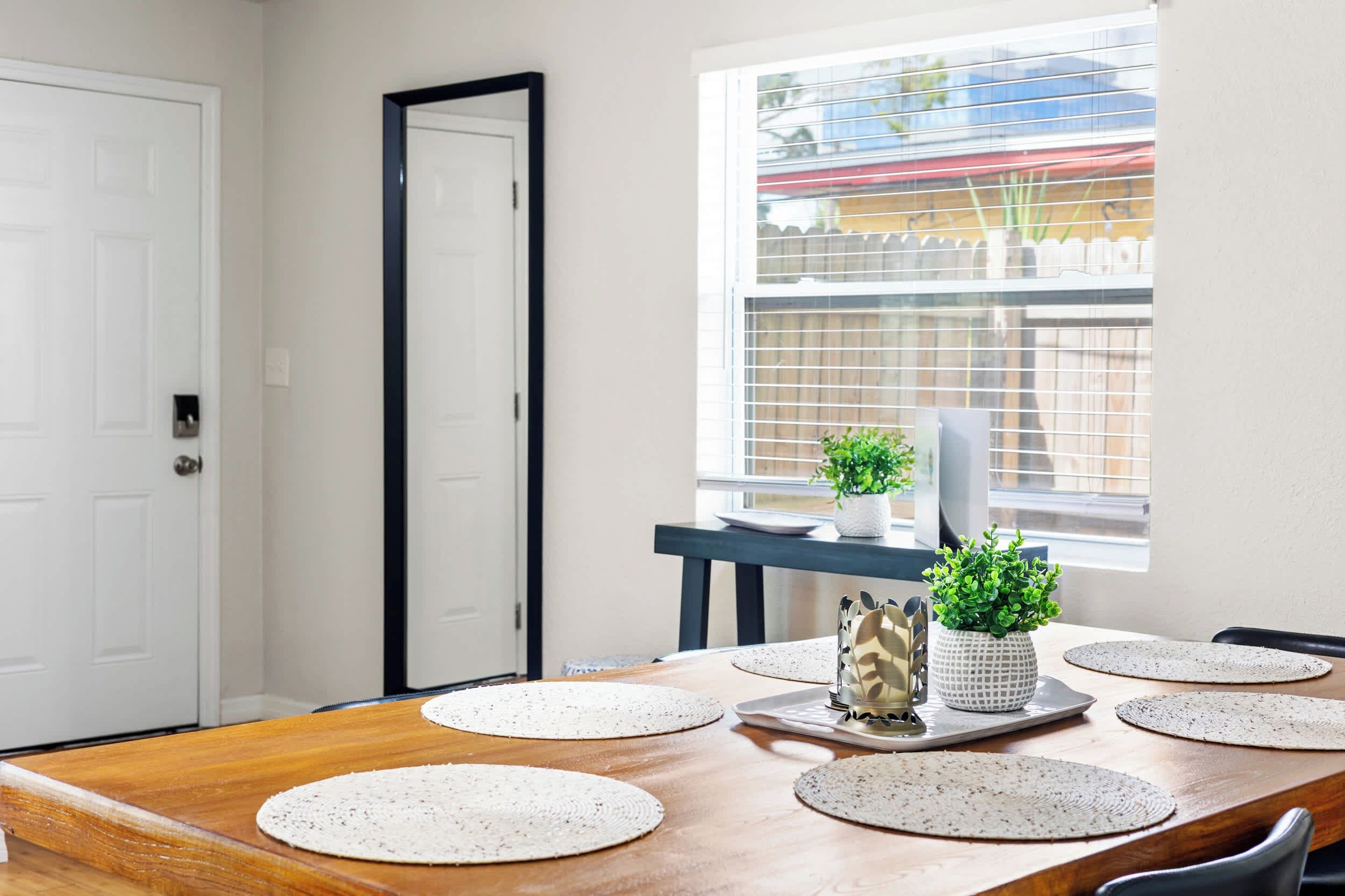 A dining area with a wooden table, placemats, a white plate, and two potted plants.