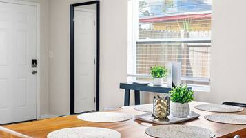 A dining area with a wooden table, placemats, a white plate, and two potted plants.