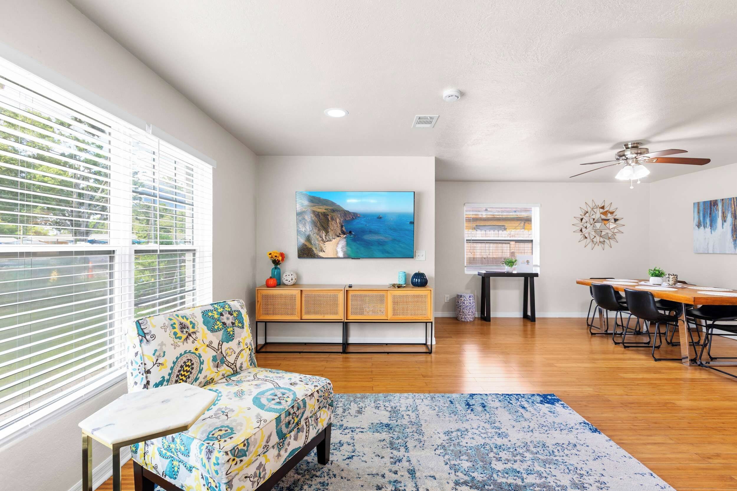 A spacious living area with a sofa, a dining table with chairs, a large painting, and a ceiling fan.