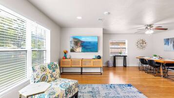 A spacious living area with a sofa, a dining table with chairs, a large painting, and a ceiling fan.