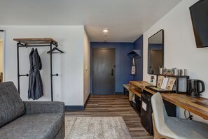 Een moderne hotelkamer met een houten bureau, een bank, een kapstok en een spiegel.