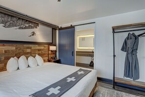 Een hotelkamer met een bed, een houten hoofdbord, een kledingrek en een zichtbare badkamer door een open deur.