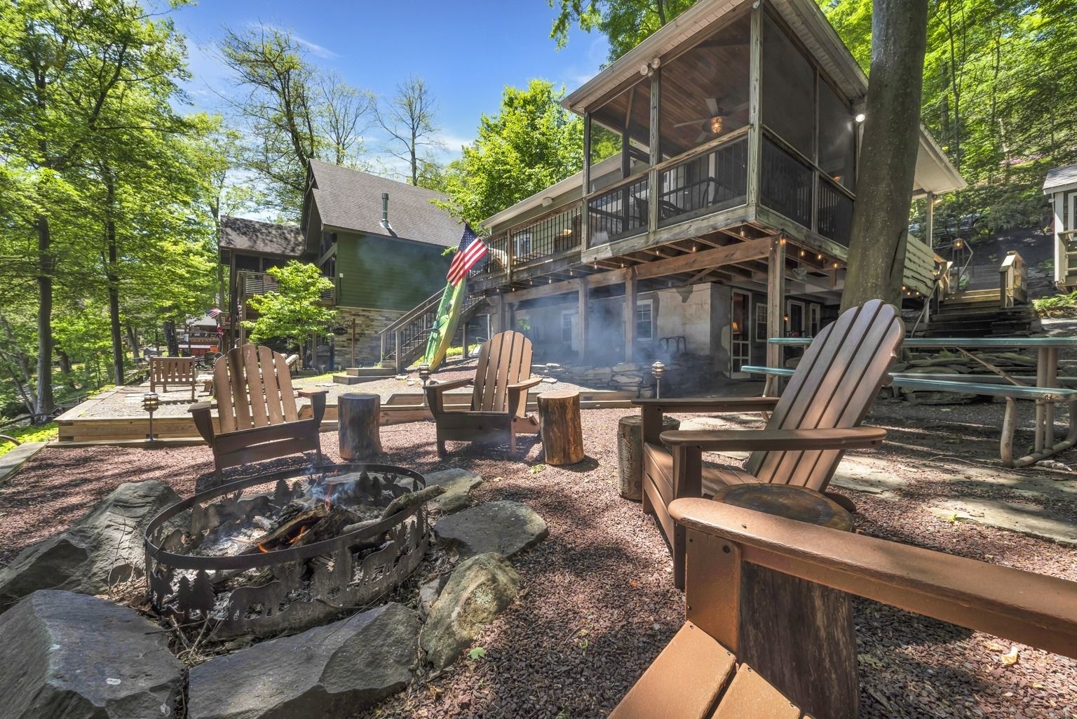 A lodge with a fire pit, Adirondack chairs, and a view of the surrounding forest.