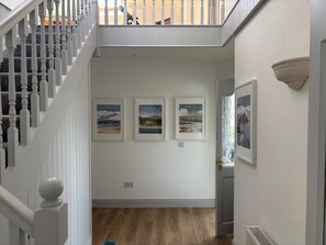 Eine Treppe mit weißen Balustraden führt zu einem Zwischenpodest mit gerahmten Kunstwerken.