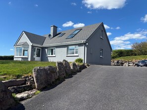Ein zweistöckiges Haus mit grauem Dach, Schornstein und einer Steinmauer davor.