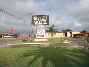 A motel sign with a parking area and a gas station in the background.