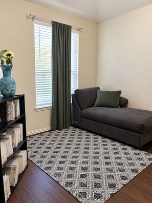 A living room with a sofa, a patterned rug, a bookshelf, and a window with curtains.