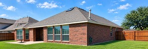 A single-story brick house with a gabled roof, a front porch, and a fenced backyard.