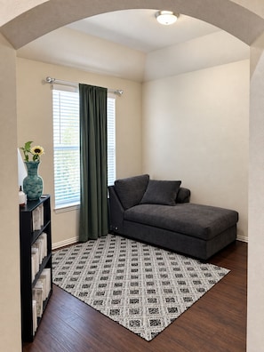A cozy corner with a grey sofa, a patterned rug, a bookshelf, and a window with curtains. - Spacious 4-bedroom house in cool Cedar Hill with AC (Cedar Hill)