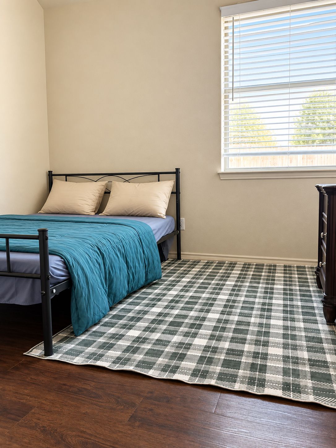 A bedroom with a bed, a window with blinds, a checkered rug, and a dresser.
