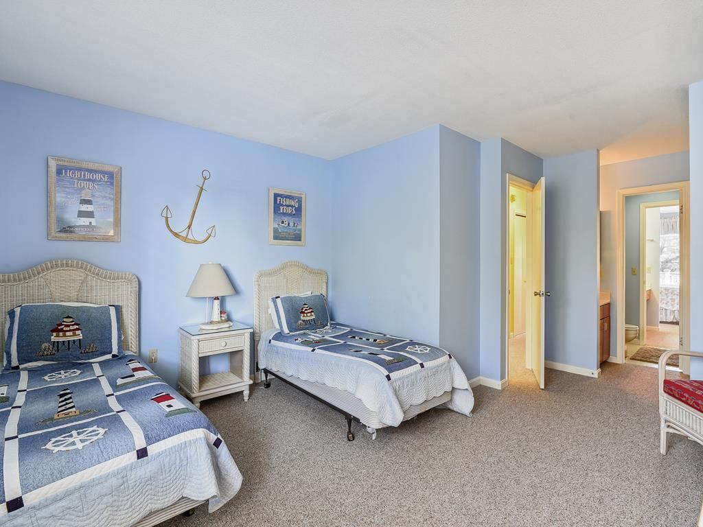 A bedroom with two beds, a nightstand, a lamp, and nautical-themed decor.