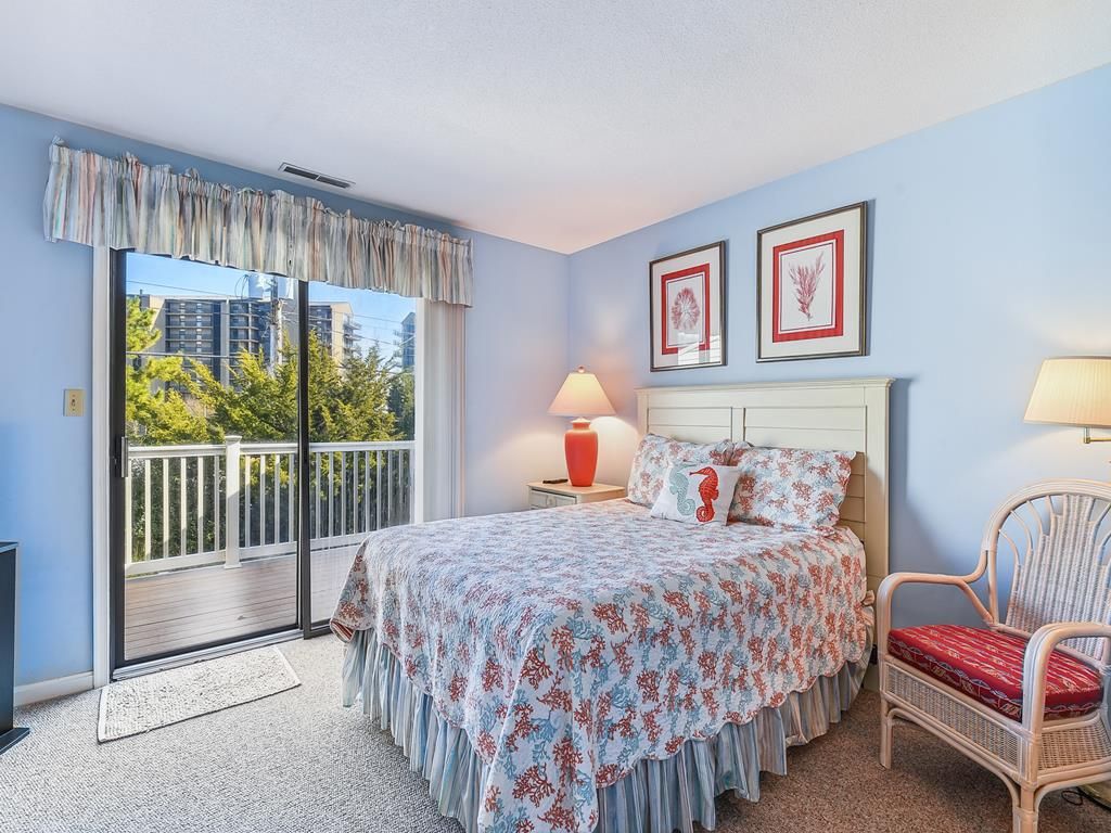 Une chambre à coucher comprenant un lit, une chaise, une table de chevet, une lampe, une fenêtre donnant sur un paysage agréable et deux tableaux encadrés accrochés au mur.