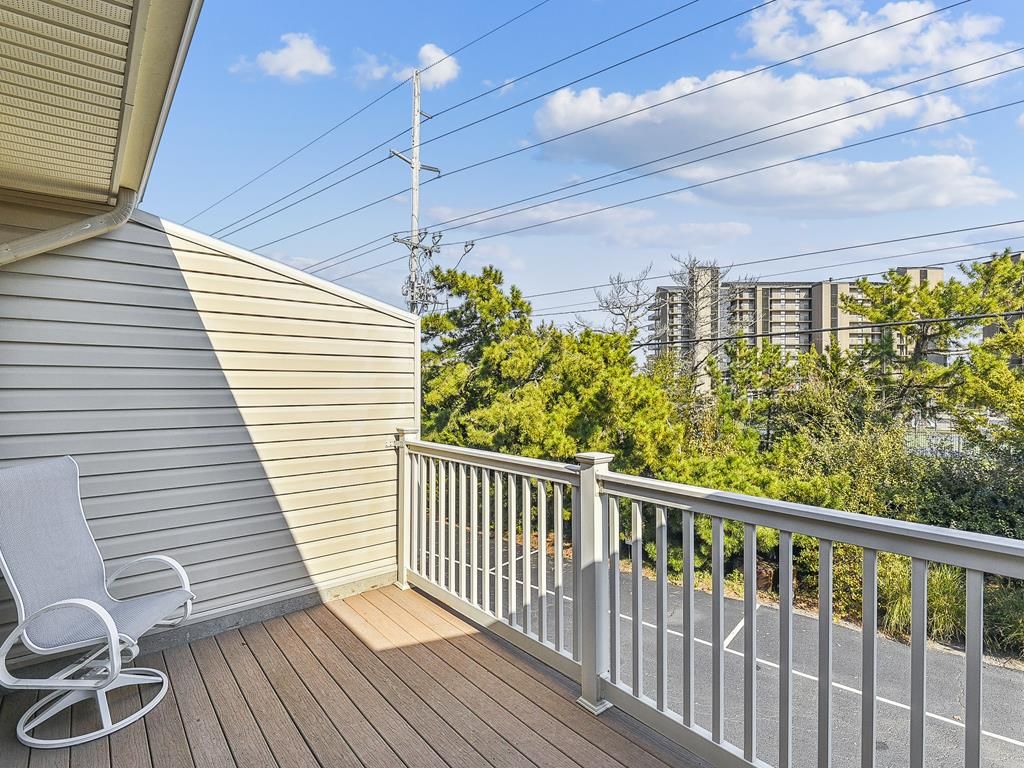 A balcony with a white railing, a white chair, and a view of a road and buildings.