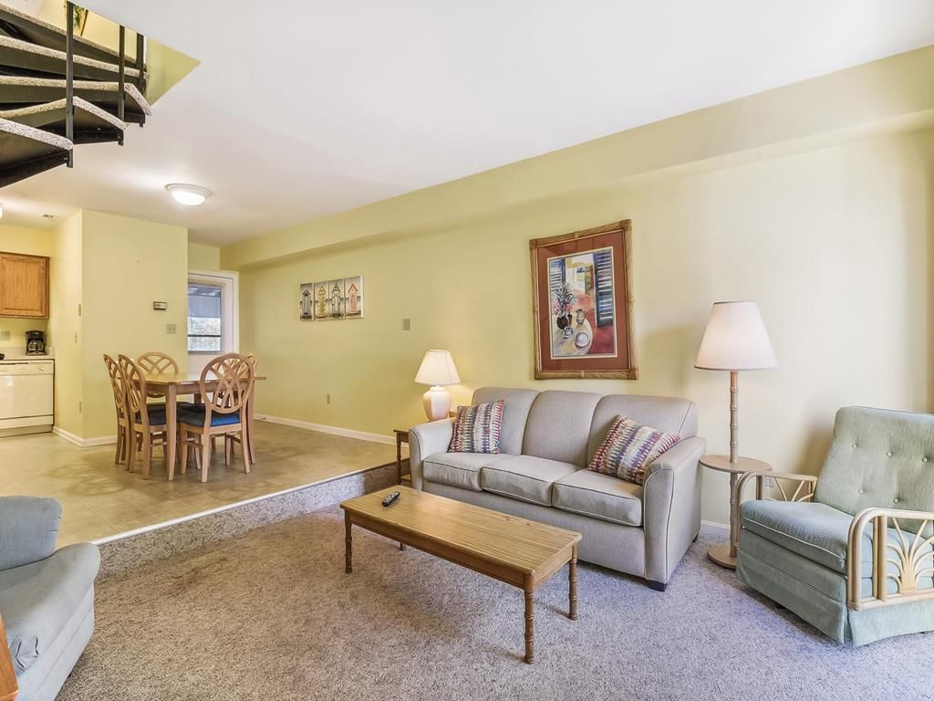 A living room with a sofa, a coffee table, a dining table with chairs, a lamp, and a painting on the wall.