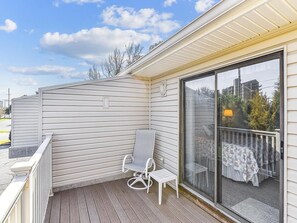 A covered outdoor area with a sliding glass door, a white chair, and a small table. - 2-Bedroom Condo w/ Private Deck near Bethany Beach (Bethany Beach)