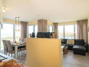 A modern living room with a dining area, a black sofa, and a kitchen island. - Holiday Apartment With 2 Bedrooms (Heiligenhafen)