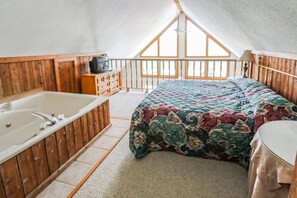 A bedroom with a large bed, a wooden bathtub, and a balcony with a wooden railing. - 1BR Condo w/ Private Balcony | Near Alpine Trails! (Helen)