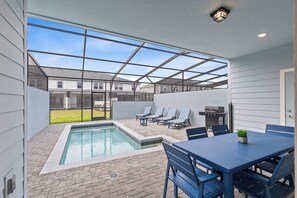 Ein überdachter Außenbereich mit Pool, Liegestühlen und Grill.