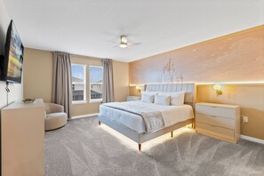 Quarto de hotel com cama, escrivaninha, cadeira, ventilador de teto e uma janela grande com cortinas.