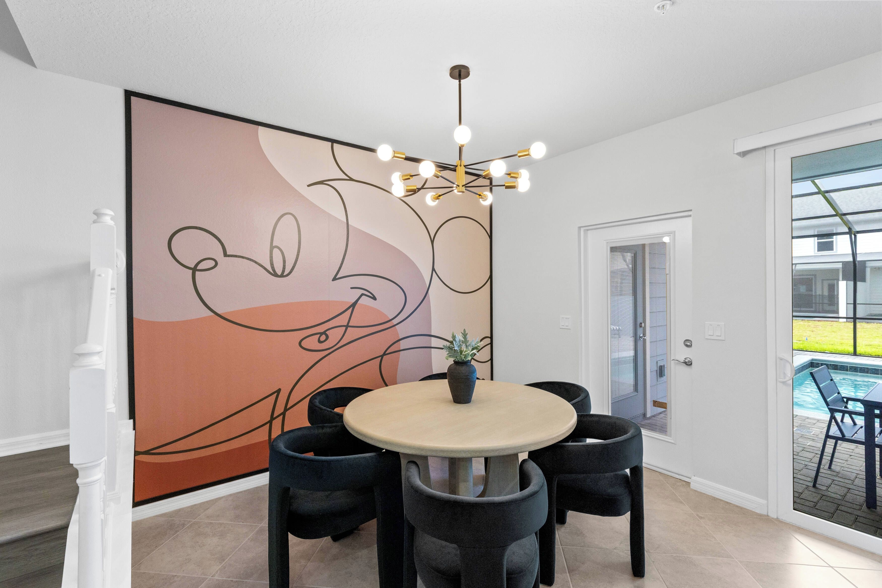 A dining area with a round table, black chairs, a large abstract painting, and a modern chandelier.