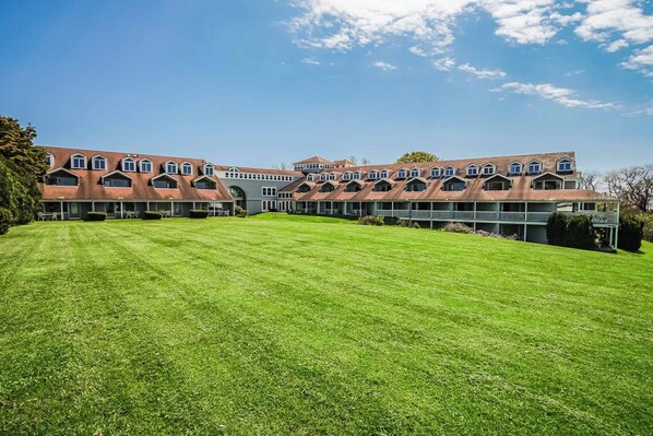 A large, multi-story building with a symmetrical facade, multiple balconies, and a well-maintained lawn in front.
