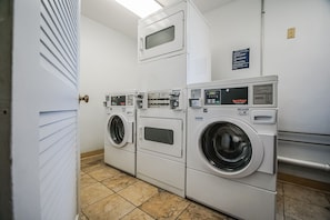 A laundry room with three stacked washers and dryers, a control panel, and a sign with operating instructions.