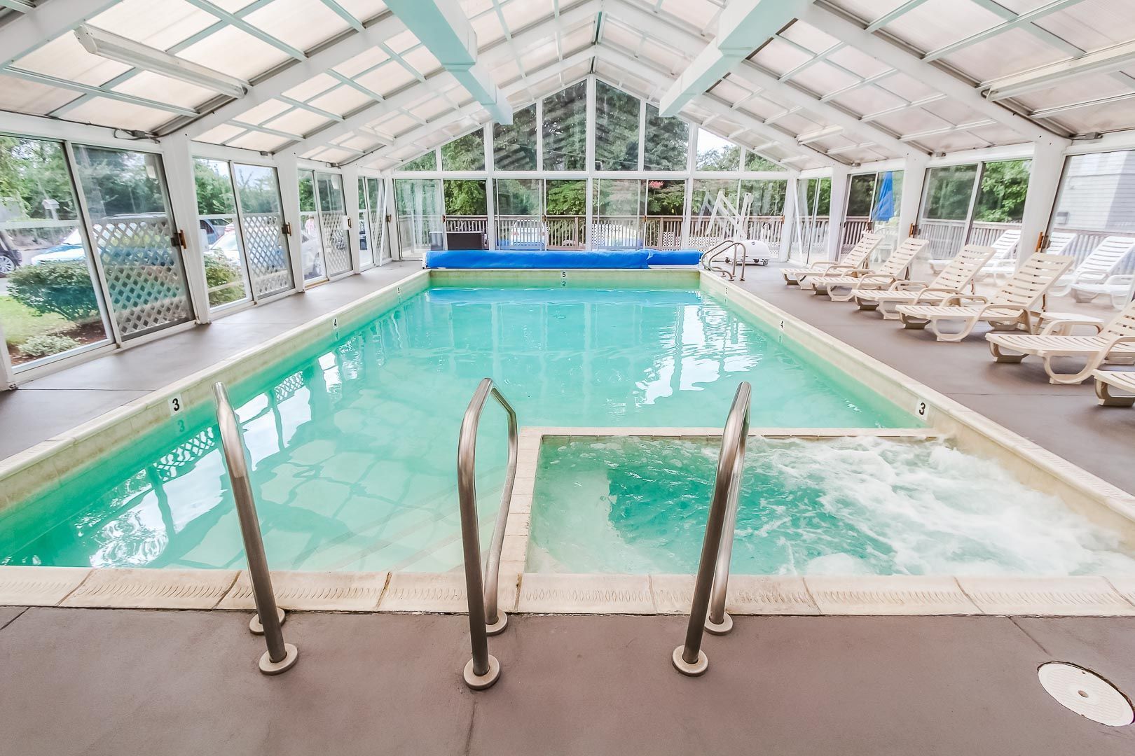 An indoor swimming pool with clear water, a blue deck area, and lounge chairs along the sides.