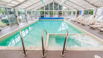 Une piscine intérieure à l’eau claire, avec une zone de pont bleu et des chaises longues disposées le long des bords.