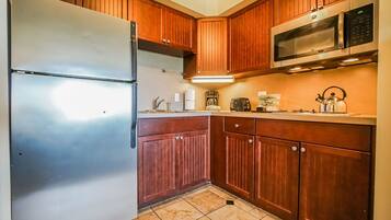 A kitchen with wooden cabinets, a stainless steel refrigerator, a microwave, a kettle, and a coffee maker.