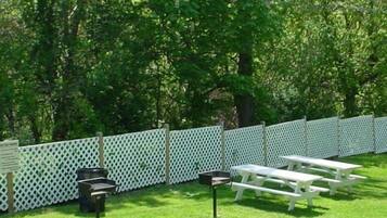 A grassy outdoor area with picnic tables and a white lattice fence.