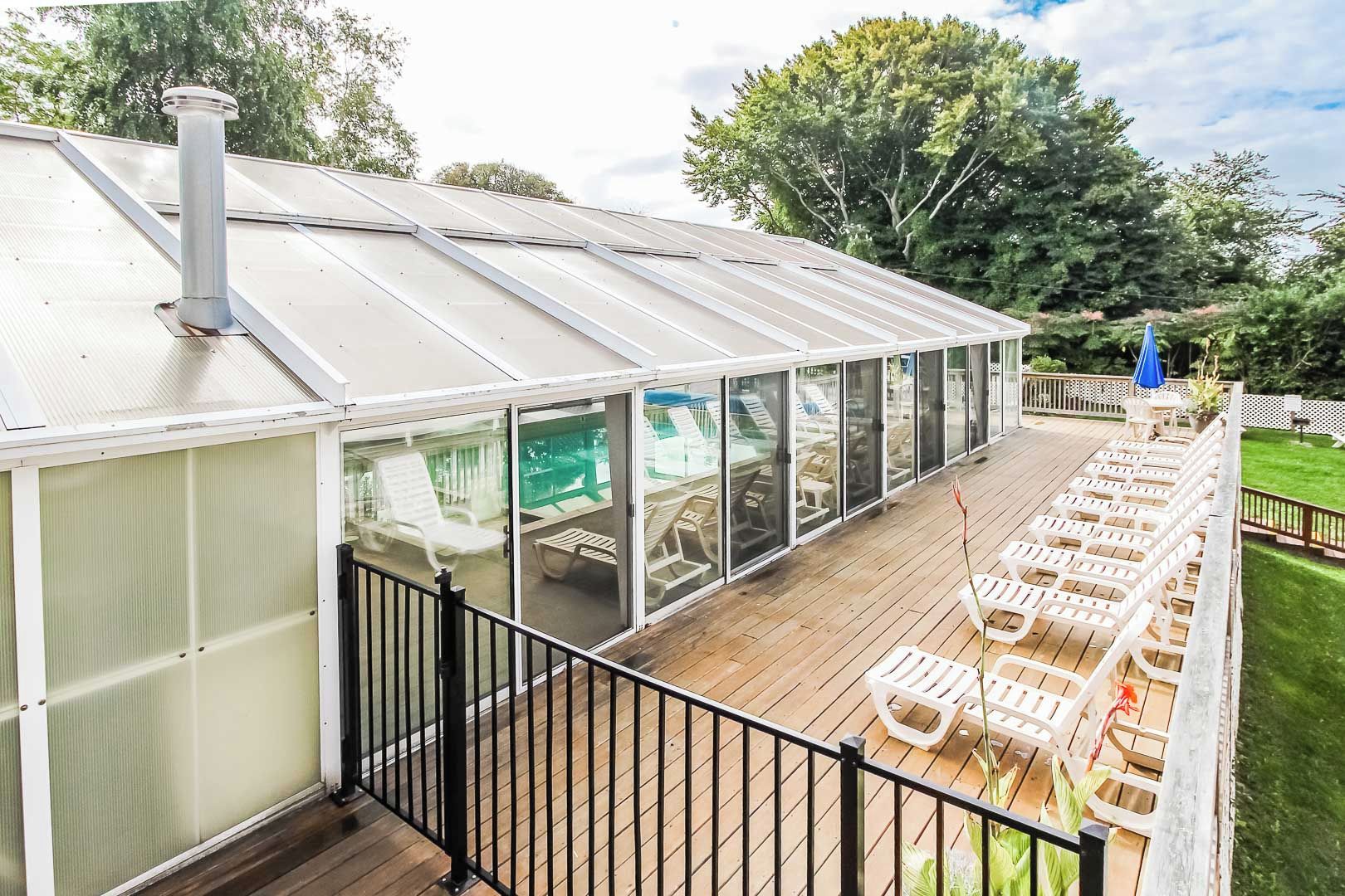 A covered outdoor deck with glass walls, wooden flooring, and lounge chairs.
