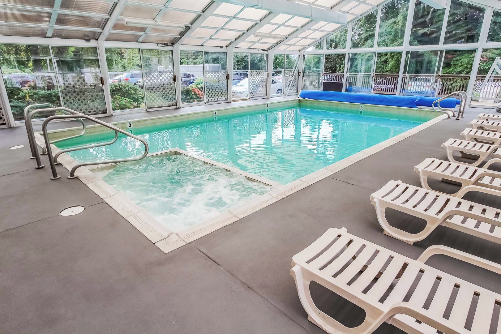 An indoor swimming pool with a covered roof, clear water, and multiple lounge chairs.