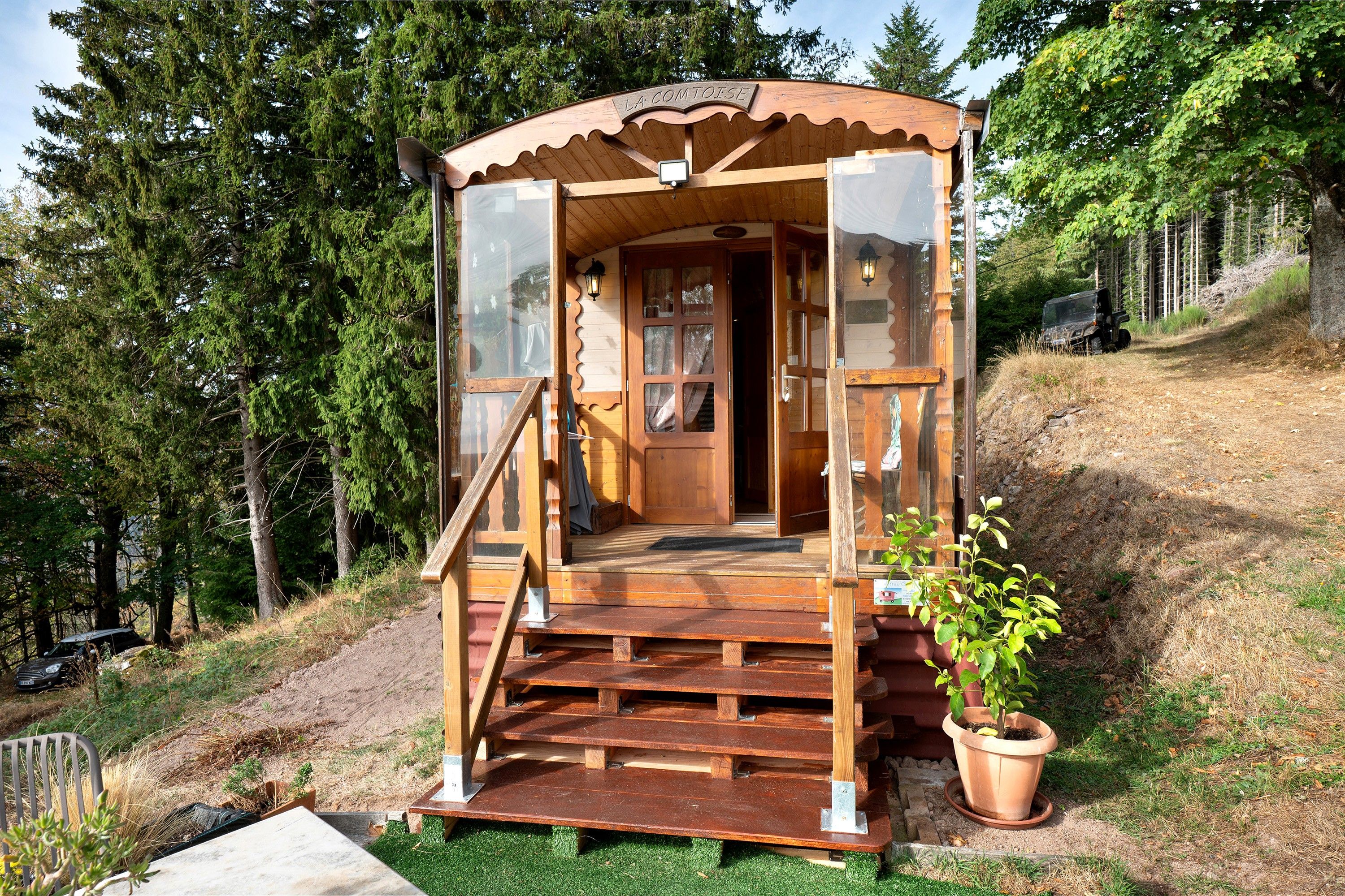 A wooden cabin with a wooden staircase leading to a door, surrounded by trees.